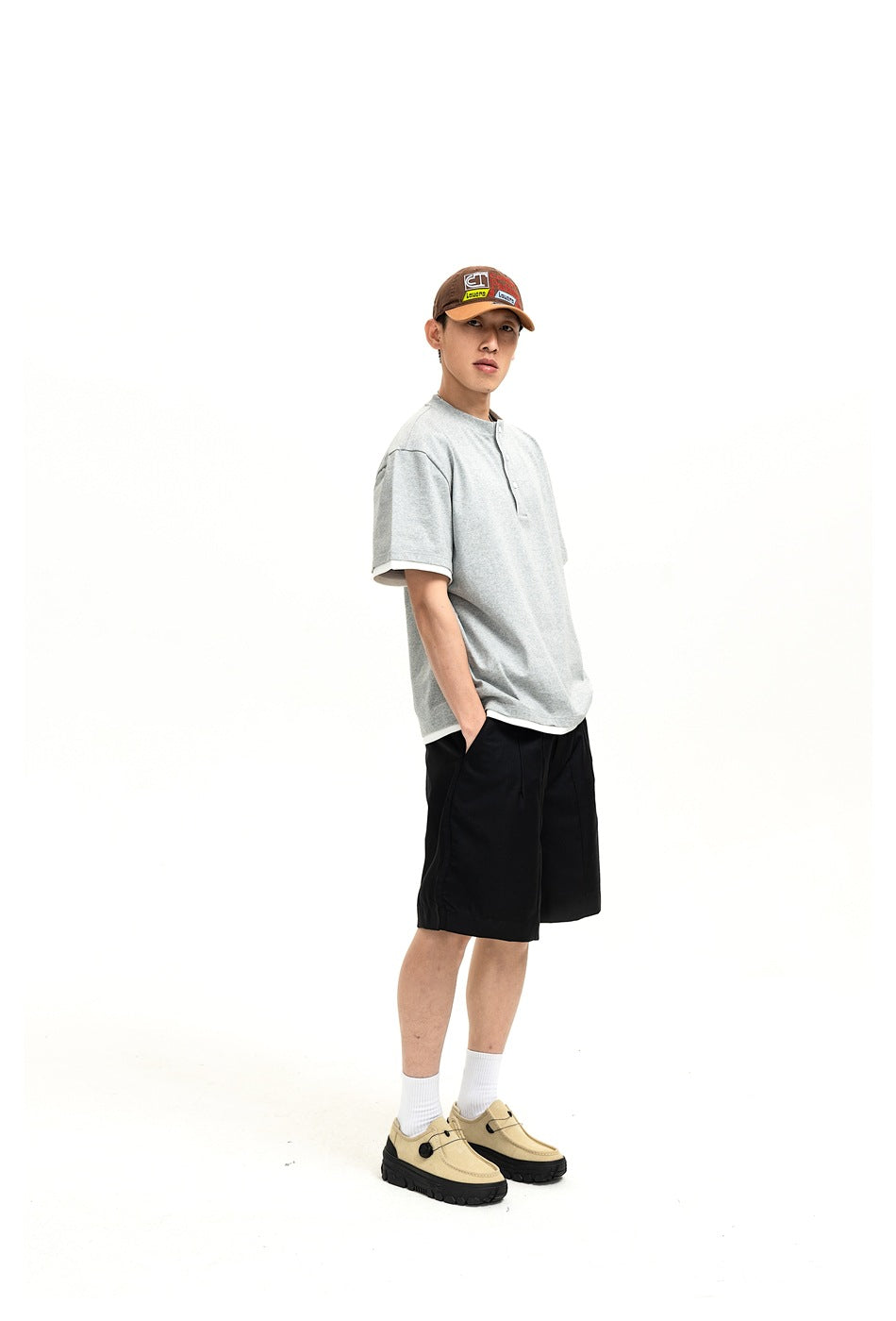 Three-quarter view of a model wearing black shorts and a light gray short-sleeve henley shirt.