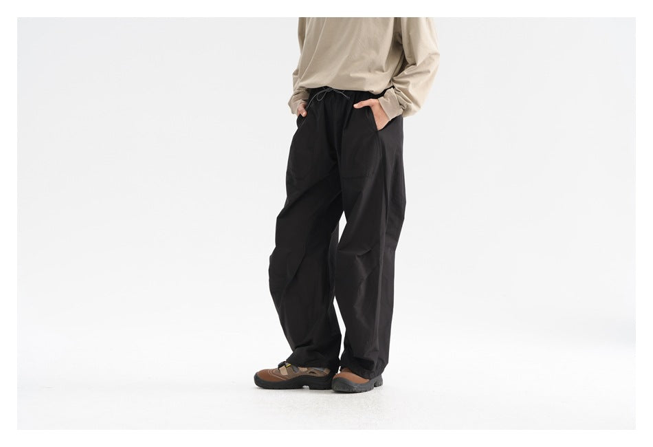 Angled front view of a person wearing loose black drawstring pants with side pockets and a beige top.