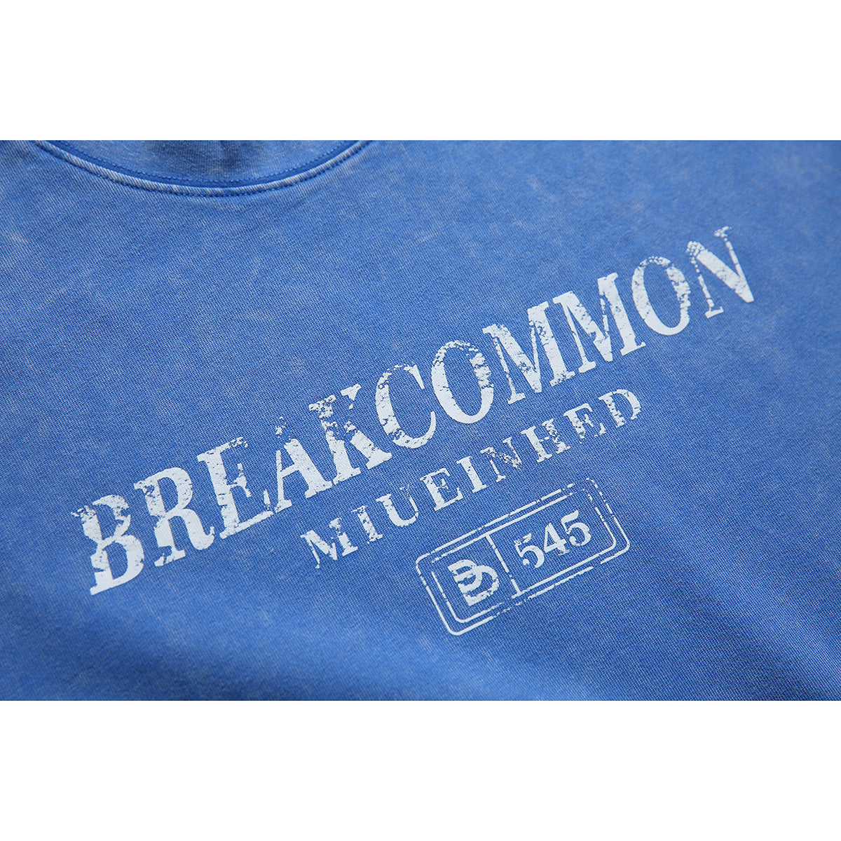Close-up of distressed white lettering and a small boxed emblem printed on blue T-shirt fabric.
