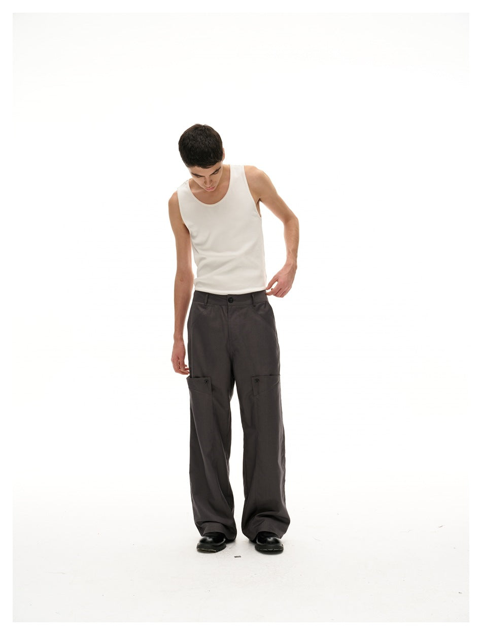 Model looking down, wearing dark gray wide-leg trousers with thigh flap pockets, a white tank top and black shoes