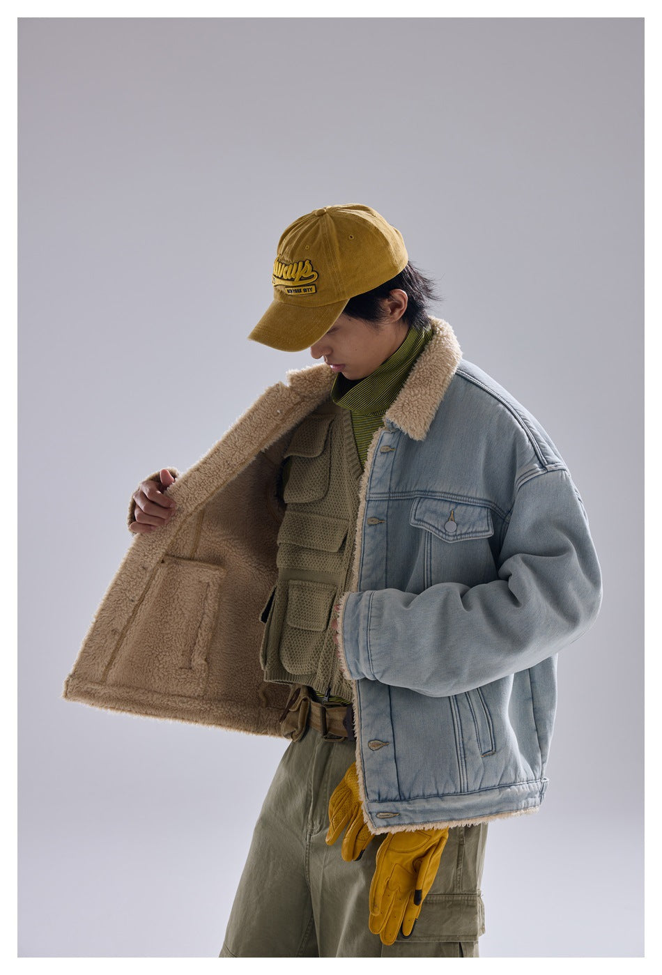 Model holds open a light blue sherpa-lined denim jacket, showing its cream lining and front pockets.
