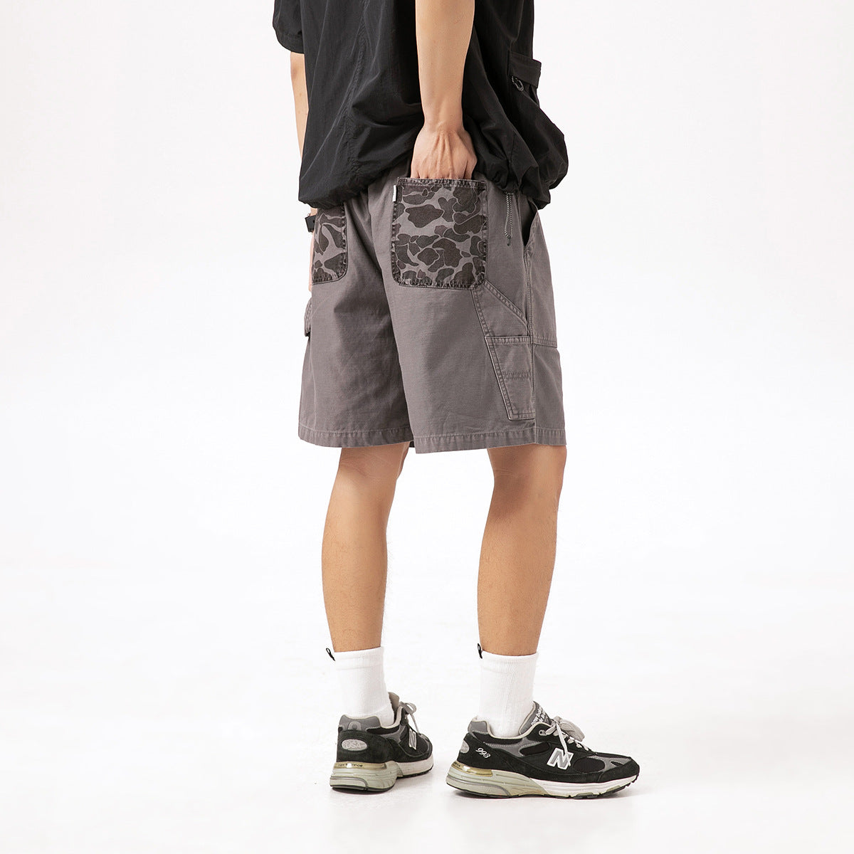 Rear view of gray cargo shorts with camouflage-print back pockets, worn by a model.