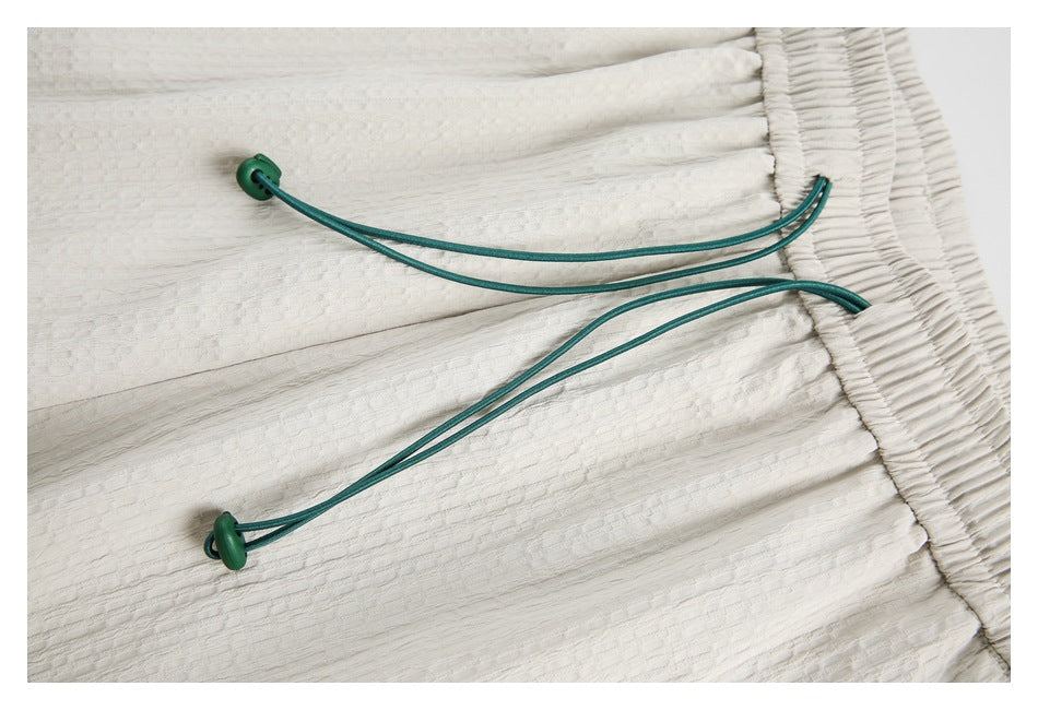 Close-up of teal drawcords and green toggles on white textured shorts.