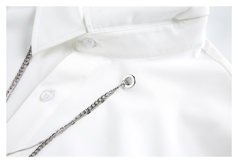 Close-up of a white collared shirt with buttons and a silver chain detail.
