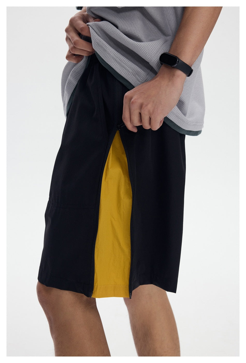 Close-up of a model wearing black shorts with an open side zipper revealing a mustard-yellow panel.