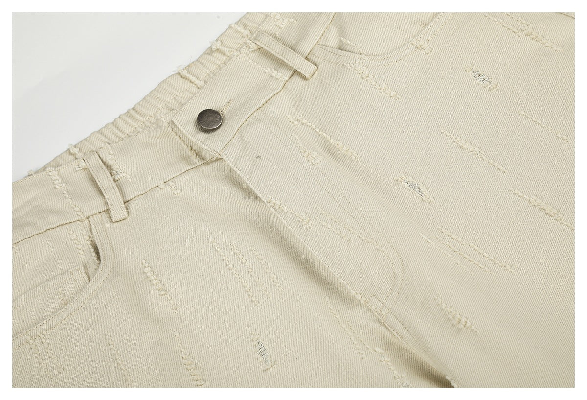 Close-up of cream trousers showing the button, belt loops, front pocket seam and raised stitch pattern.
