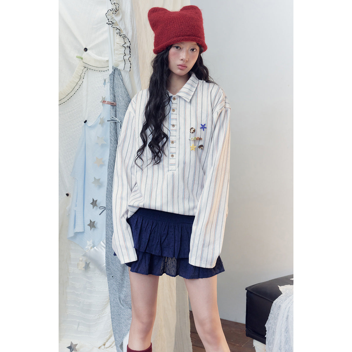 Model wearing a white shirt with thin blue and red stripes and playful chest embellishments, paired with a navy tiered skirt.
