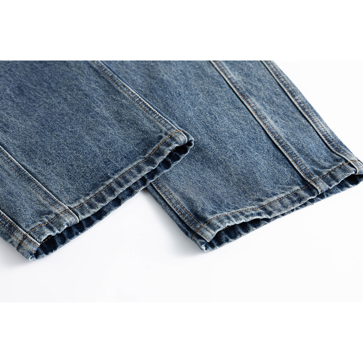 Close-up of two blue washed denim jean legs showing stitched hems.