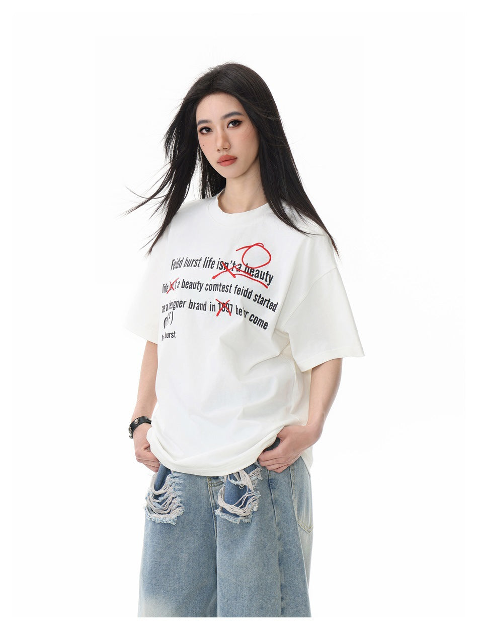Close three-quarter view of model in white T-shirt with black slogan text and red scribbles, with distressed jeans