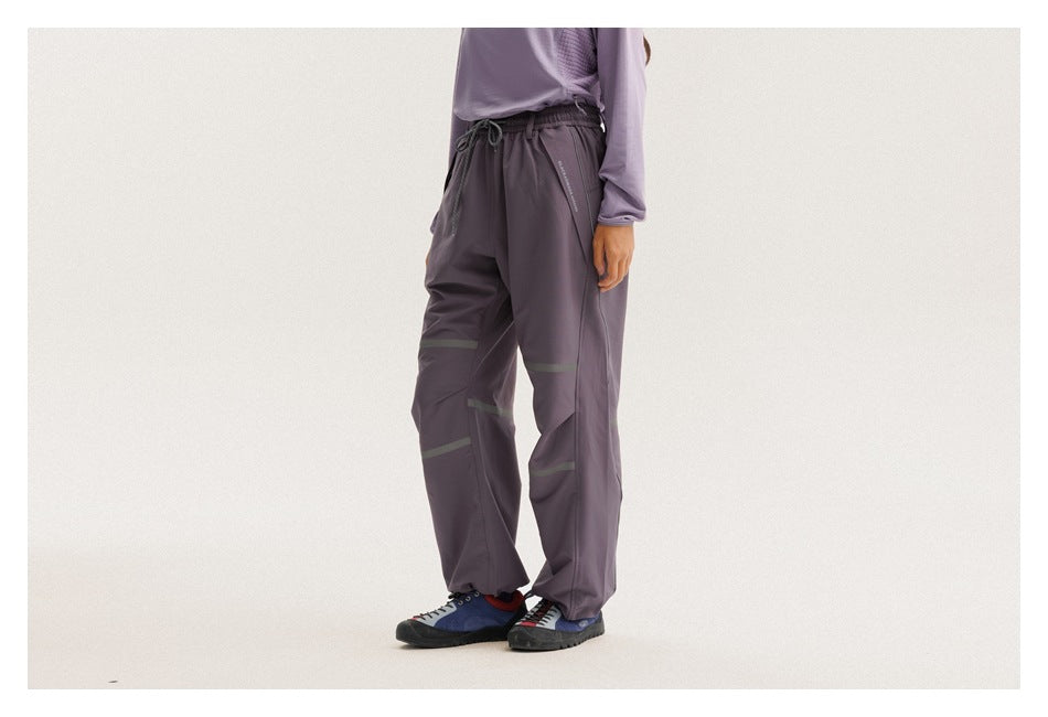 Side view of a model wearing loose dark purple drawstring pants with muted reflective bands and gathered ankles.
