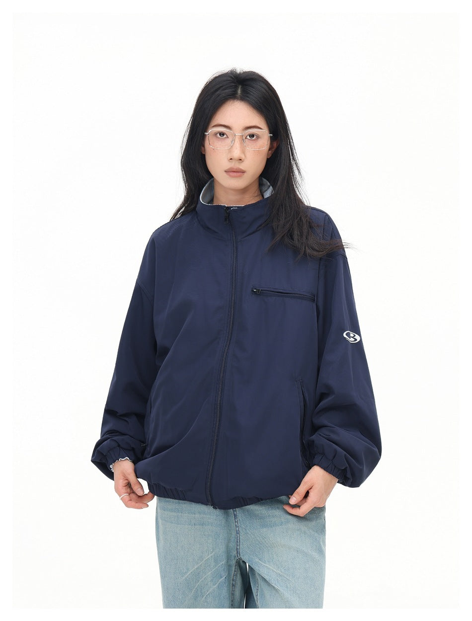 Front view of a model in a navy zip jacket with a stand collar, chest pocket and white sleeve emblem.