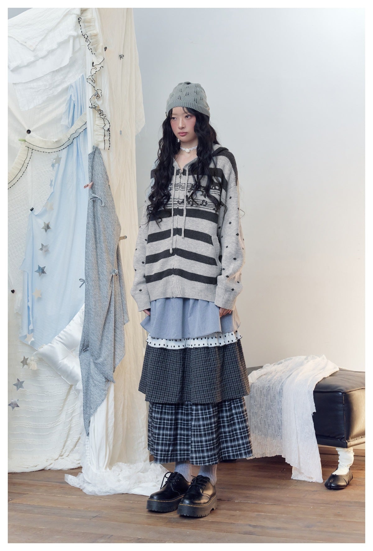 Model in gray striped zip hooded knit cardigan with music-note band and dotted sleeves, angled view with layered skirt