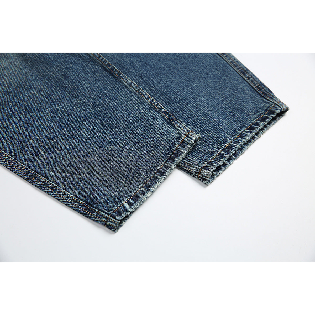 Close-up of the stitched hems on the legs of blue-wash jeans.