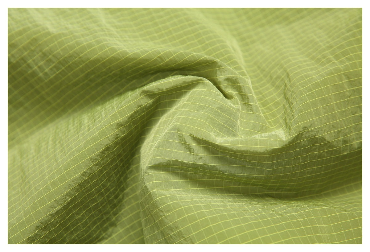Close-up of the olive-green jacket fabric showing its fine yellow grid pattern and seams.