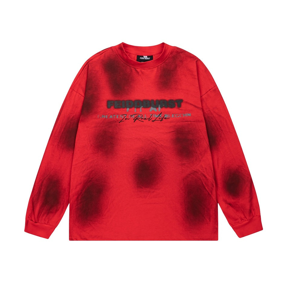 Red long-sleeve crew-neck top with dark blurred spots and a chest wordmark print, flat lay front view