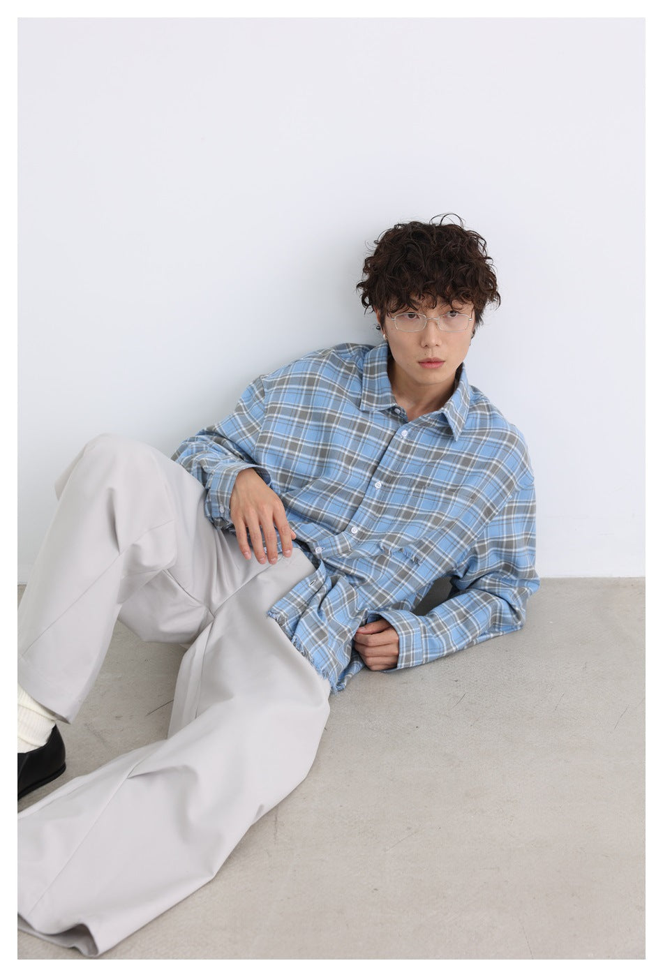 Model reclining in a blue plaid button-up shirt with a frayed chest pocket and hem.
