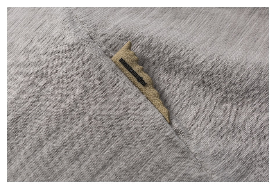 Close-up of a small tan leather-like logo patch on light gray textured fabric.