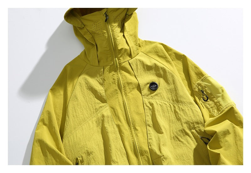 Close view of the yellow jacket’s front zipper, chest badge, hood, and zippered sleeve pocket.