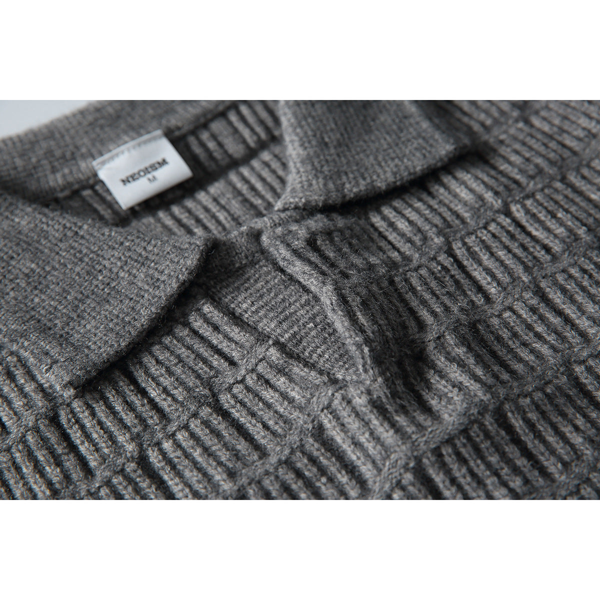 Close-up of a gray textured knit sweater showing its collar, placket, and sewn neck label.