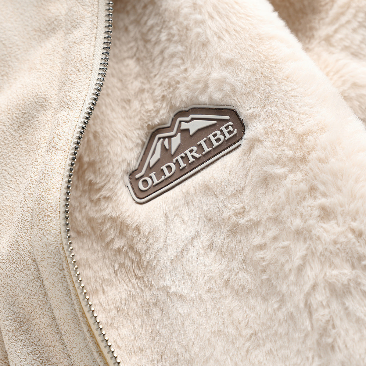 Close-up of an ivory faux-fur jacket showing its zipper and an OLDTRIBE chest patch.
