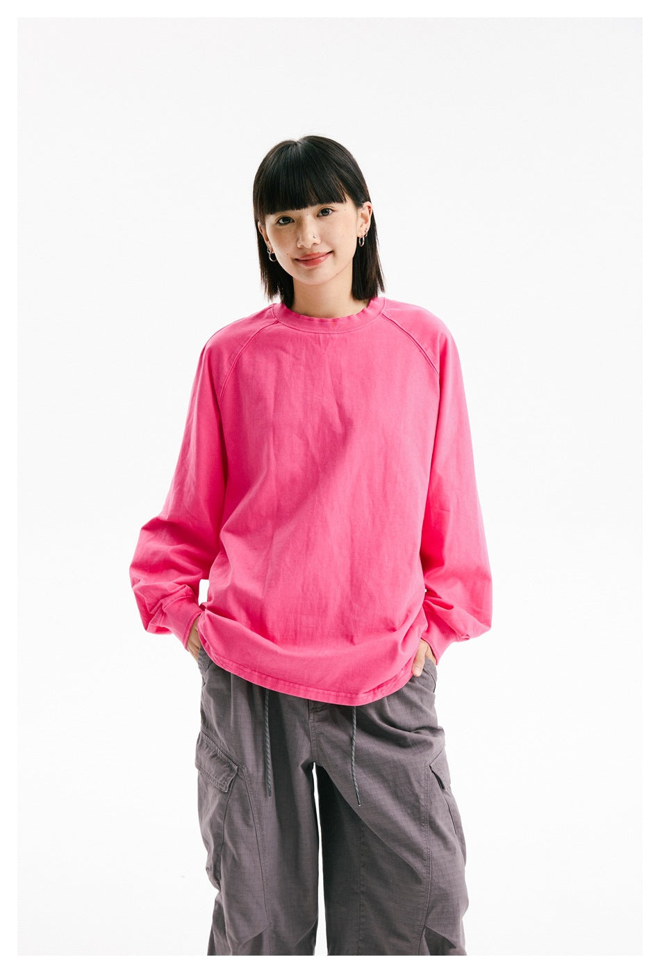Model wearing an oversized bright pink long-sleeve crewneck and gray cargo pants, shown from the front.
