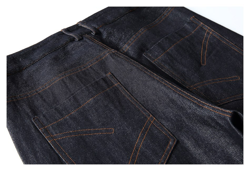 Partial rear view of dark jeans laid flat, showing two back pockets and orange stitching.