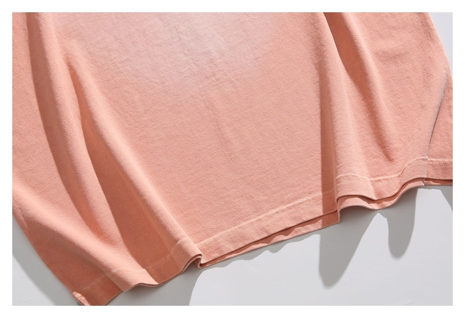 Partial view of a peach T-shirt body, short sleeve, and stitched bottom hem.