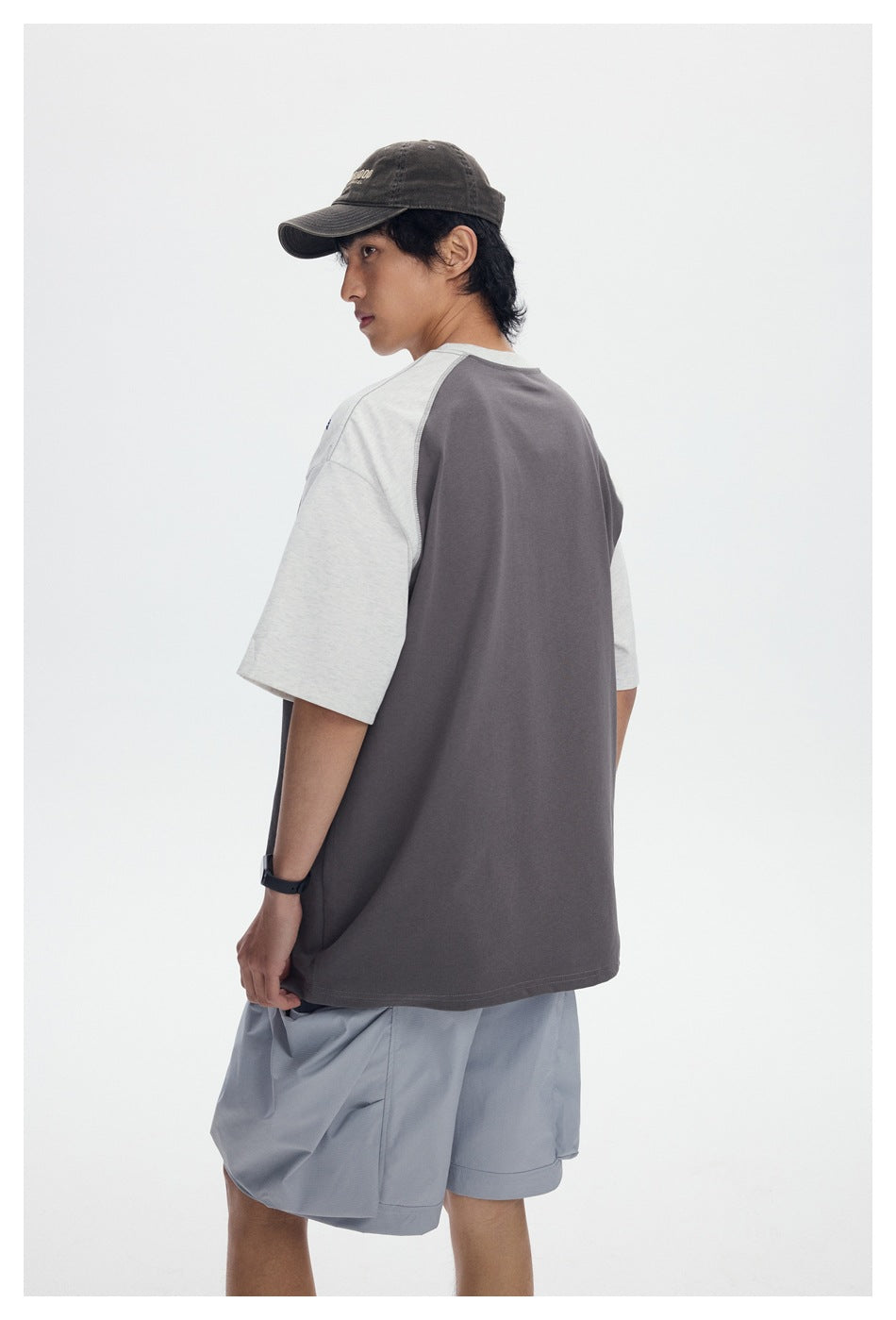 Back view of a model wearing a charcoal T-shirt with light gray raglan sleeves.