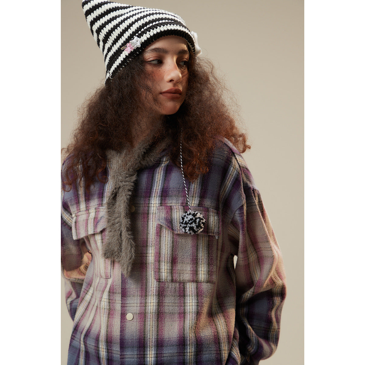Close view of a model wearing a purple plaid shirt jacket with flap pockets and a black-and-white striped beanie.
