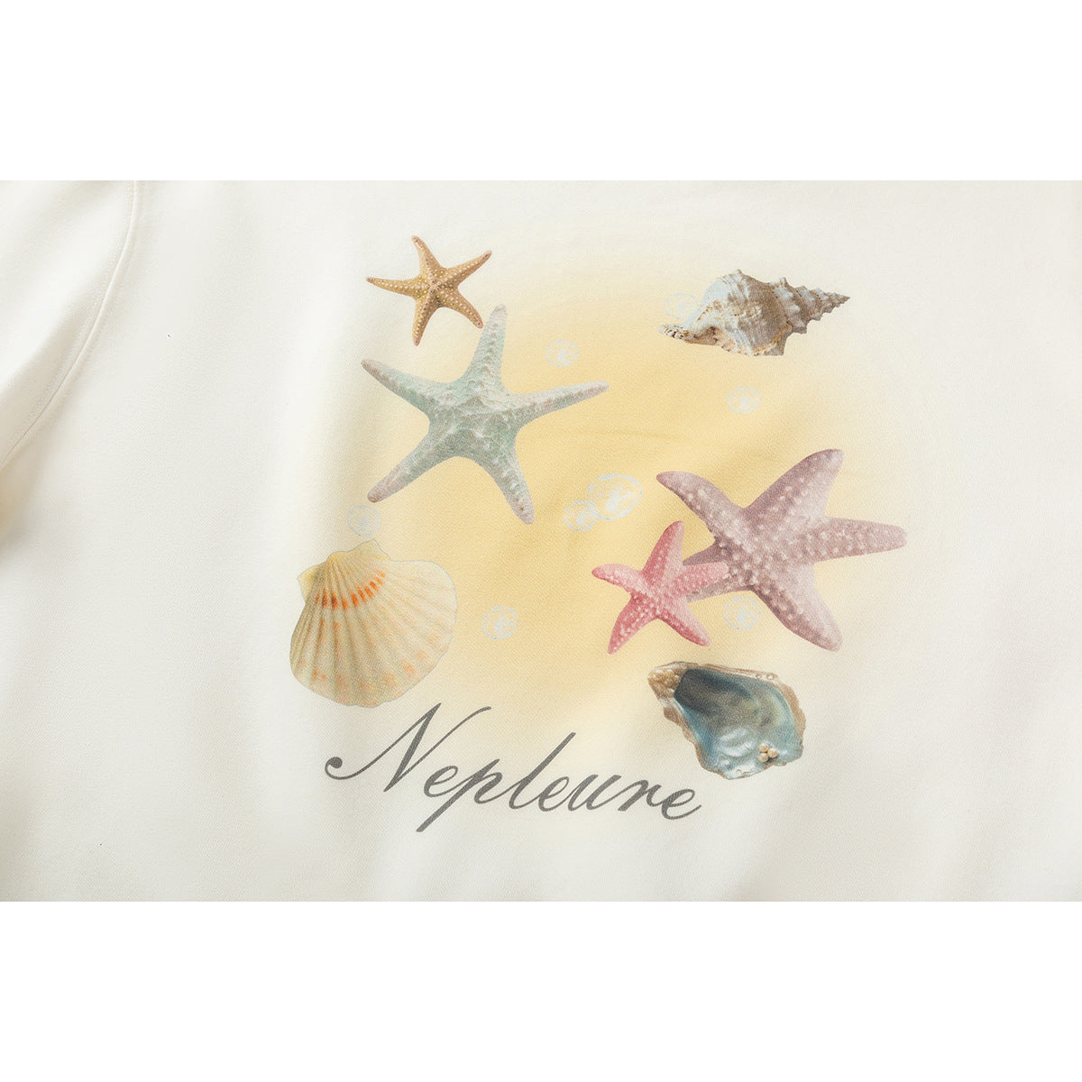 Close-up of a cream sweatshirt print featuring starfish, seashells, bubbles, and the word “Neptune.”