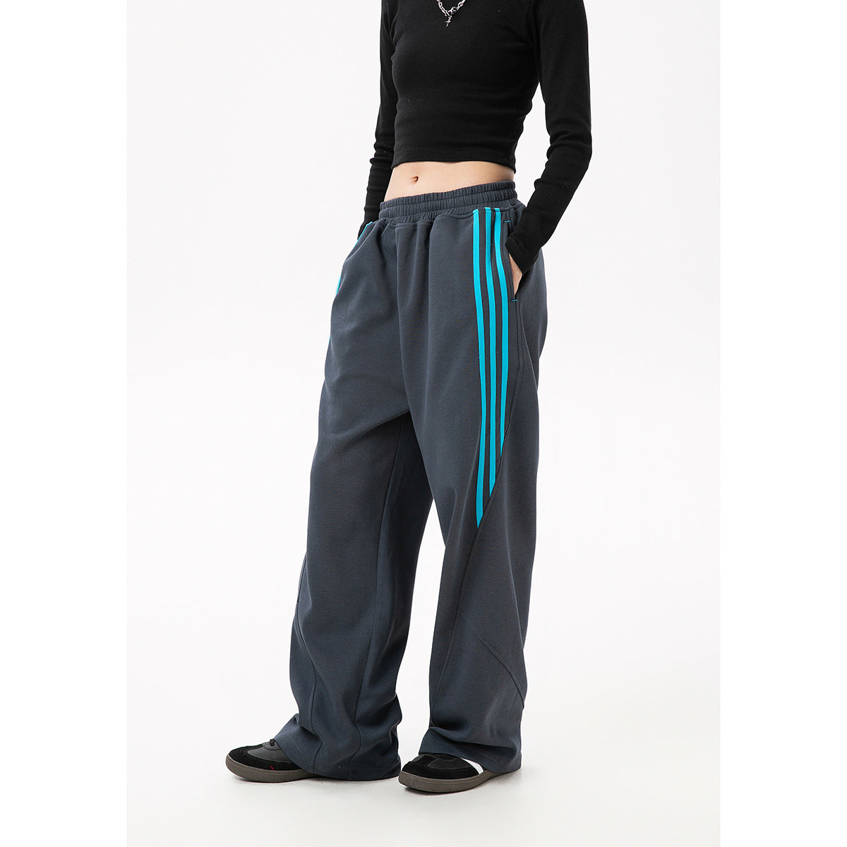 Angled view of charcoal wide-leg track pants with turquoise side stripes and pockets, worn by a model.