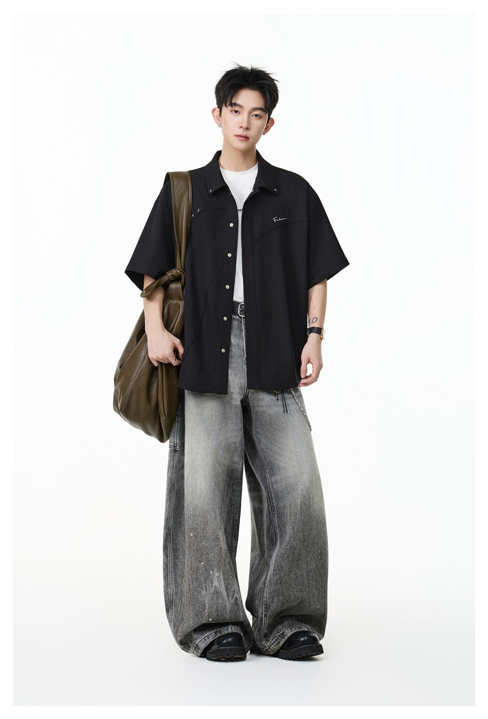 Model wearing an oversized black short-sleeve button-up shirt with curved seams and small chest embellishments.