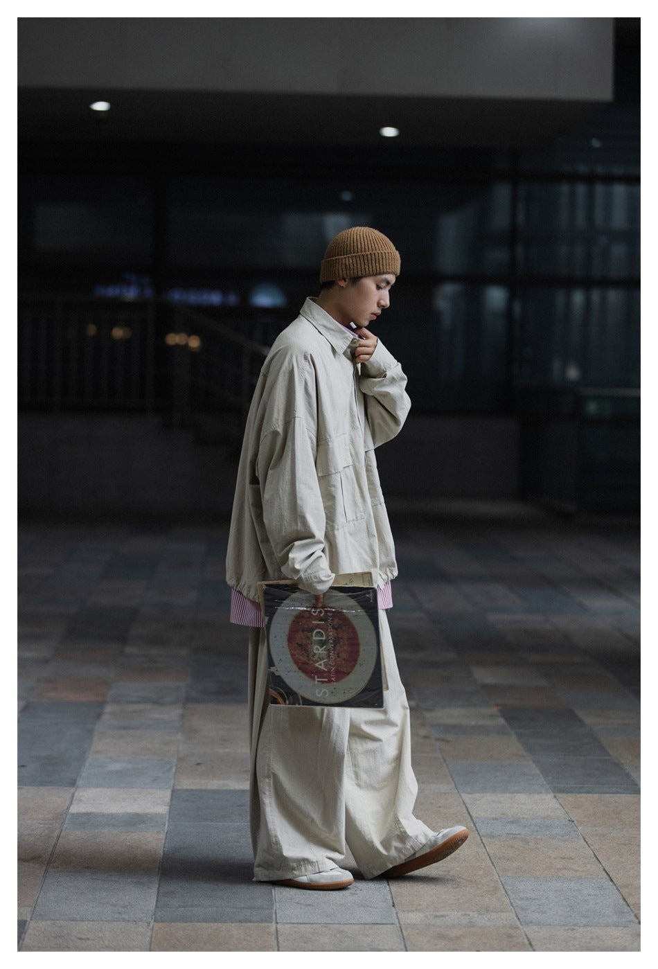 Side view of a model wearing a light gray oversized jacket and wide-leg trousers with a pink striped shirt.