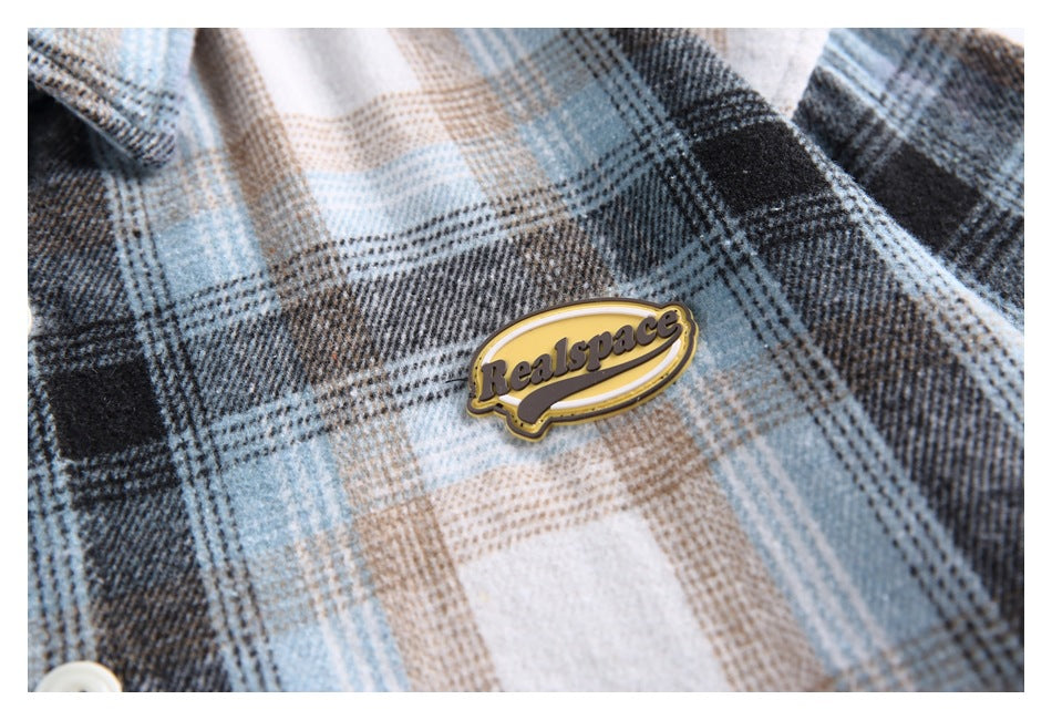 Close-up of a yellow logo patch on blue, gray and beige plaid fabric.