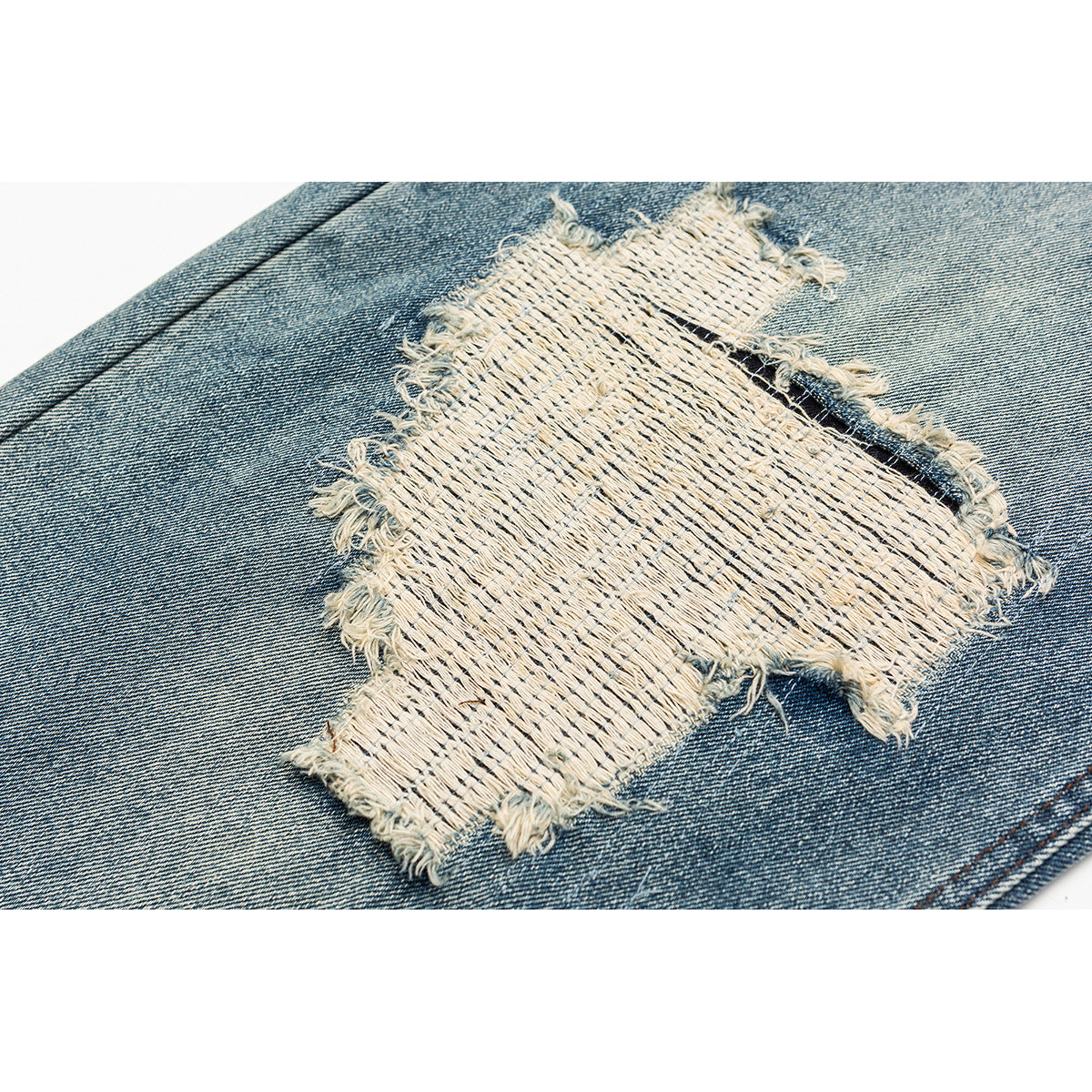 Close-up of a large frayed, cream-colored woven repair patch on faded blue denim.