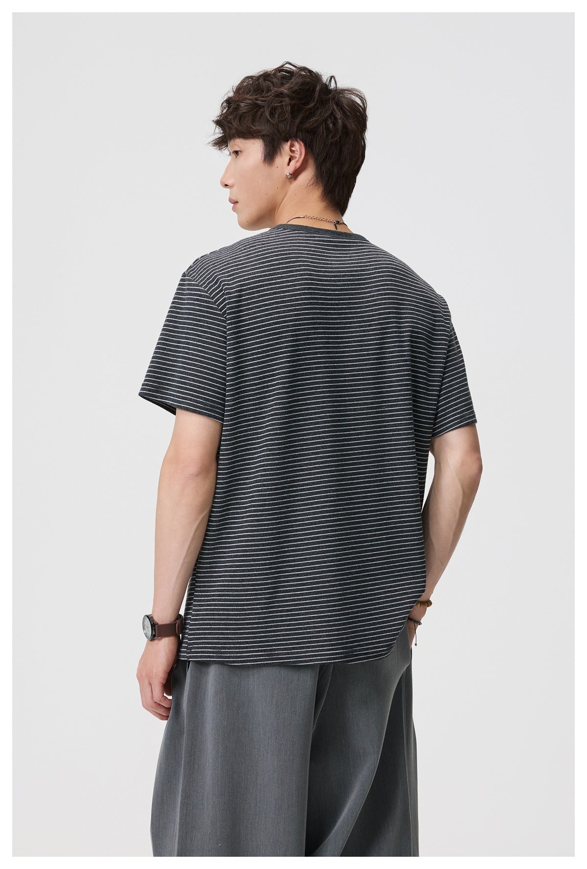 Rear view of a model wearing a charcoal T-shirt with fine light horizontal stripes.