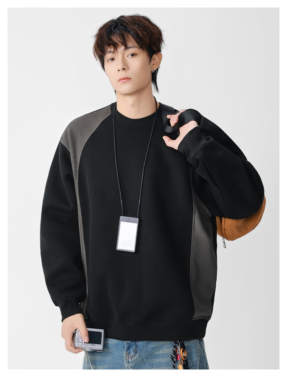 Model wearing an oversized black crewneck sweatshirt with textured charcoal shoulder and side panels.