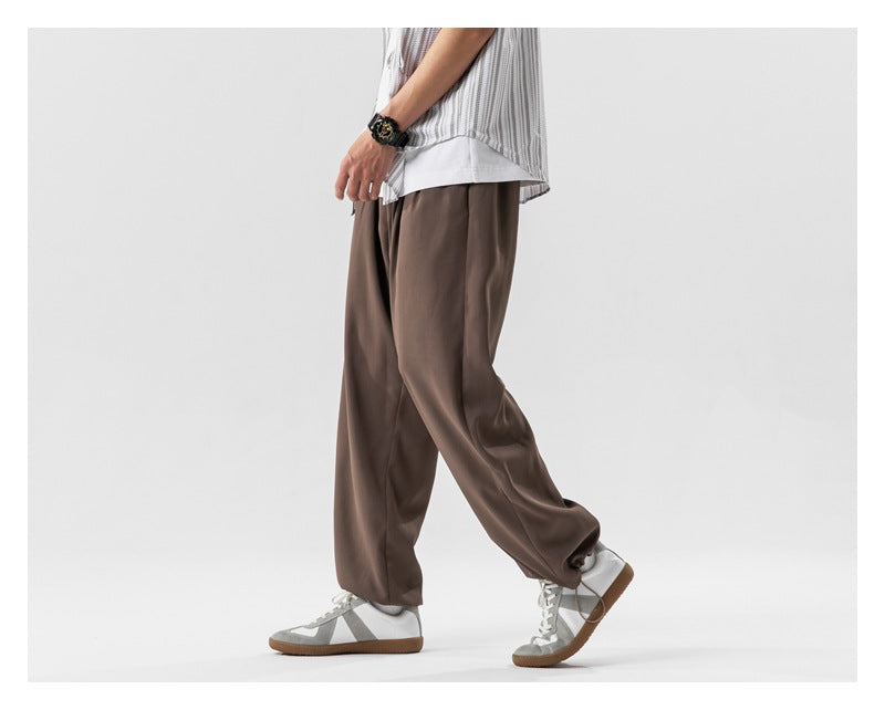 Side view of a model wearing loose brown pants with gray sneakers.