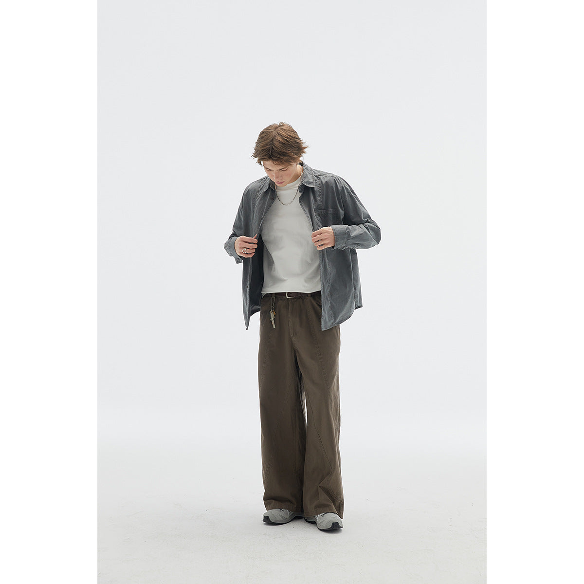 Model wears dark olive wide-leg trousers with a charcoal button-up overshirt, white T-shirt and gray sneakers.