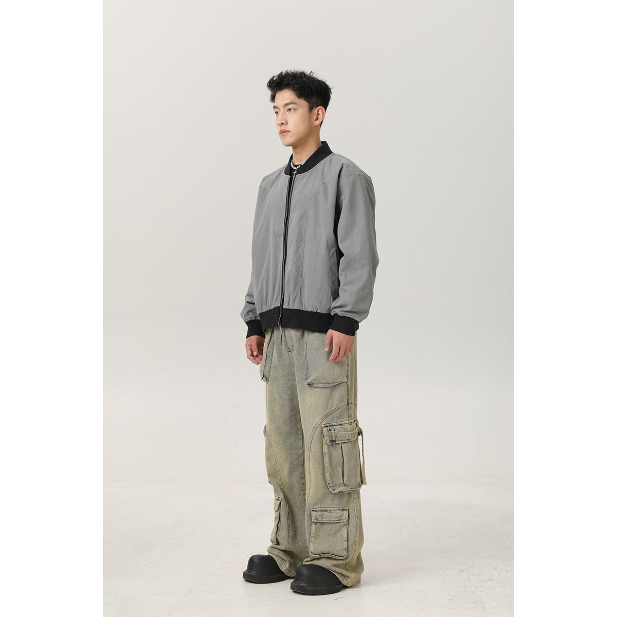 Full-length view of a model wearing a gray bomber jacket with black ribbed collar, cuffs and hem.