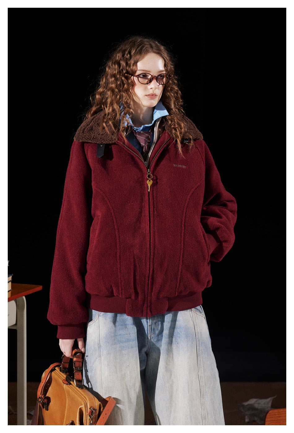 Model wearing a burgundy zip jacket with a brown sherpa collar, shown with light-wash wide jeans.