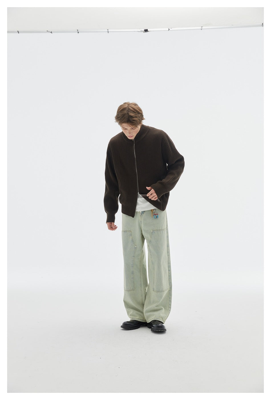 Model wearing a dark brown ribbed zip cardigan, looking down while adjusting its hem.