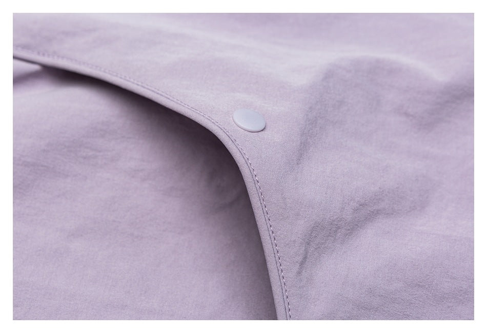 Close-up of a pale lavender shirt's curved edge, stitching, and matching round snap button.