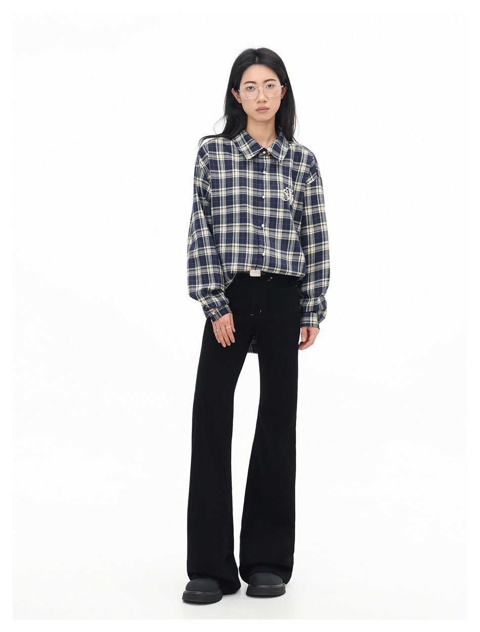 Model wearing a navy plaid button-up shirt with a beaded chest motif, buttoned, with black flared pants and black shoes