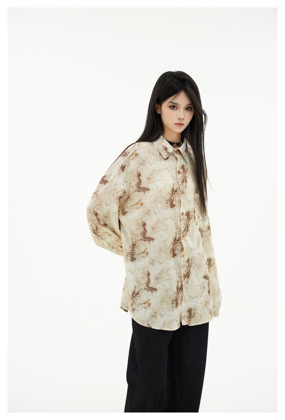 Model wearing an oversized cream button-up shirt with brown marbled print and black trousers, front view.