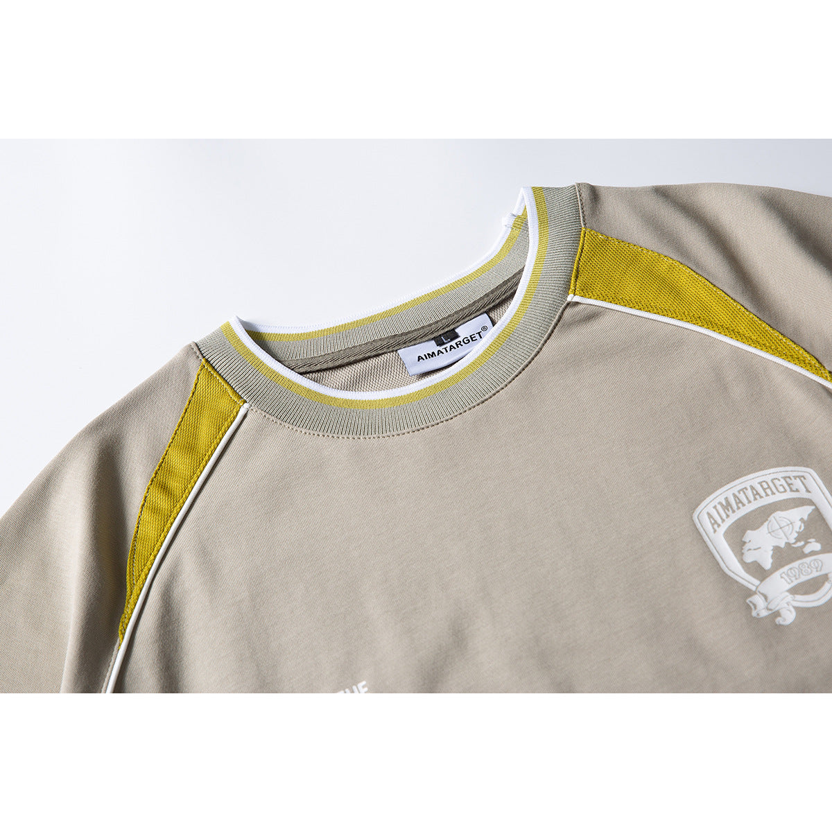 Close-up of a taupe T-shirt neckline with yellow trim and a white chest crest.