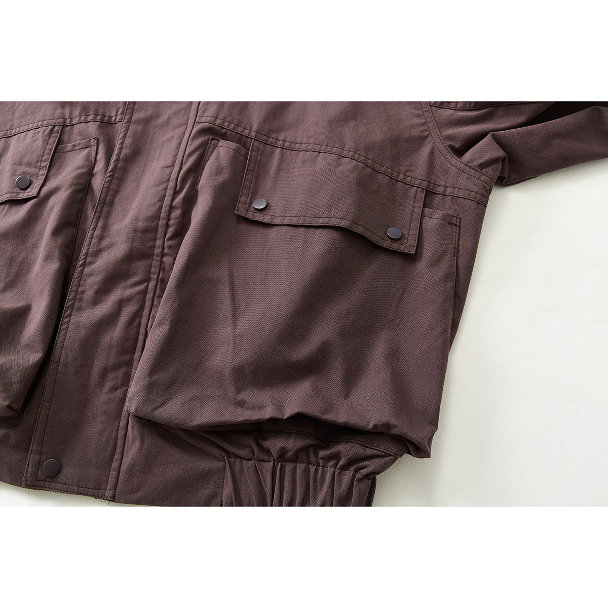 Close-up of a plum jacket's flap pockets, snap buttons, seams, and gathered hem.