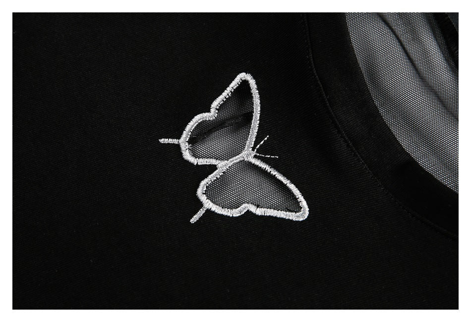 Close-up of a white embroidered butterfly on the black top beside a sheer mesh panel.