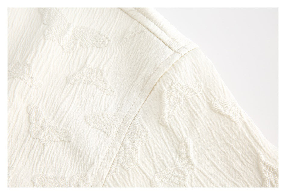Close-up of the ivory garment's shoulder seam and raised textured pattern.
