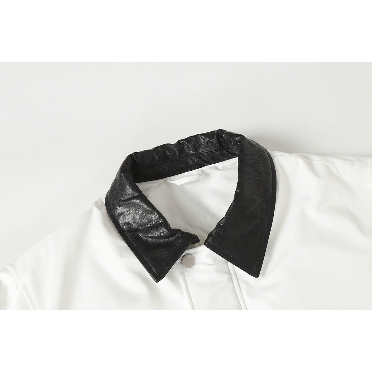 Close-up of a white jacket with a wide black collar and silver snap fastening.